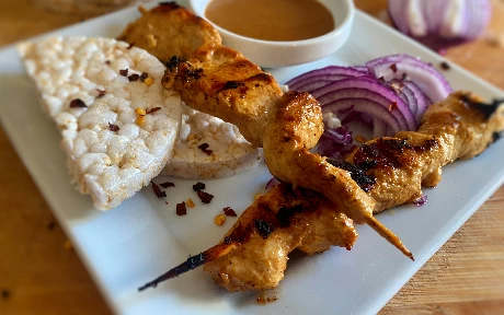 two chicken skewers with a peanut sauce